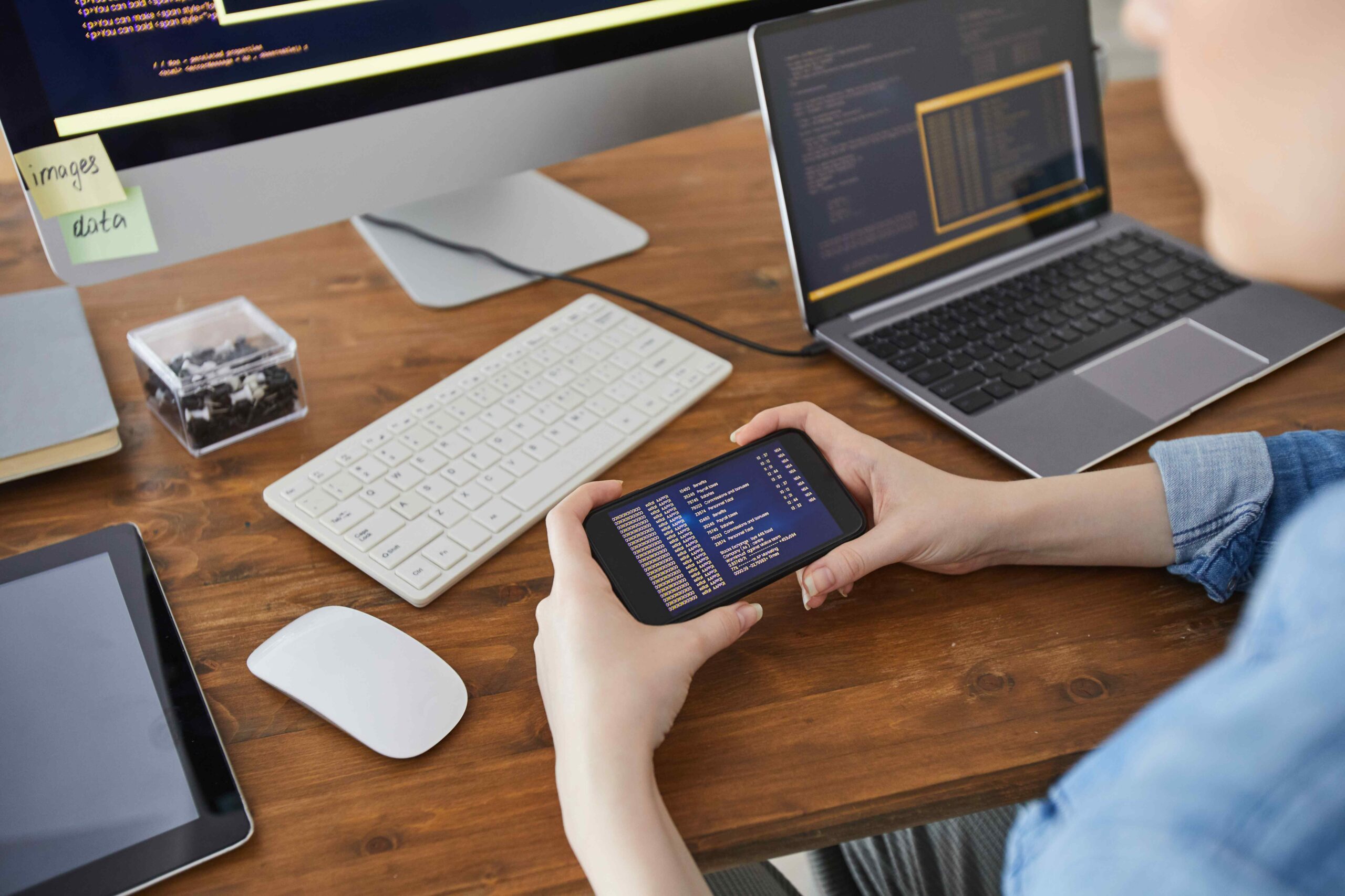 high-angle-closeup-female-hands-holding-smartphone-with-code-screen-while-working-desk-office-female-it-developer-concept-copy-space (1)