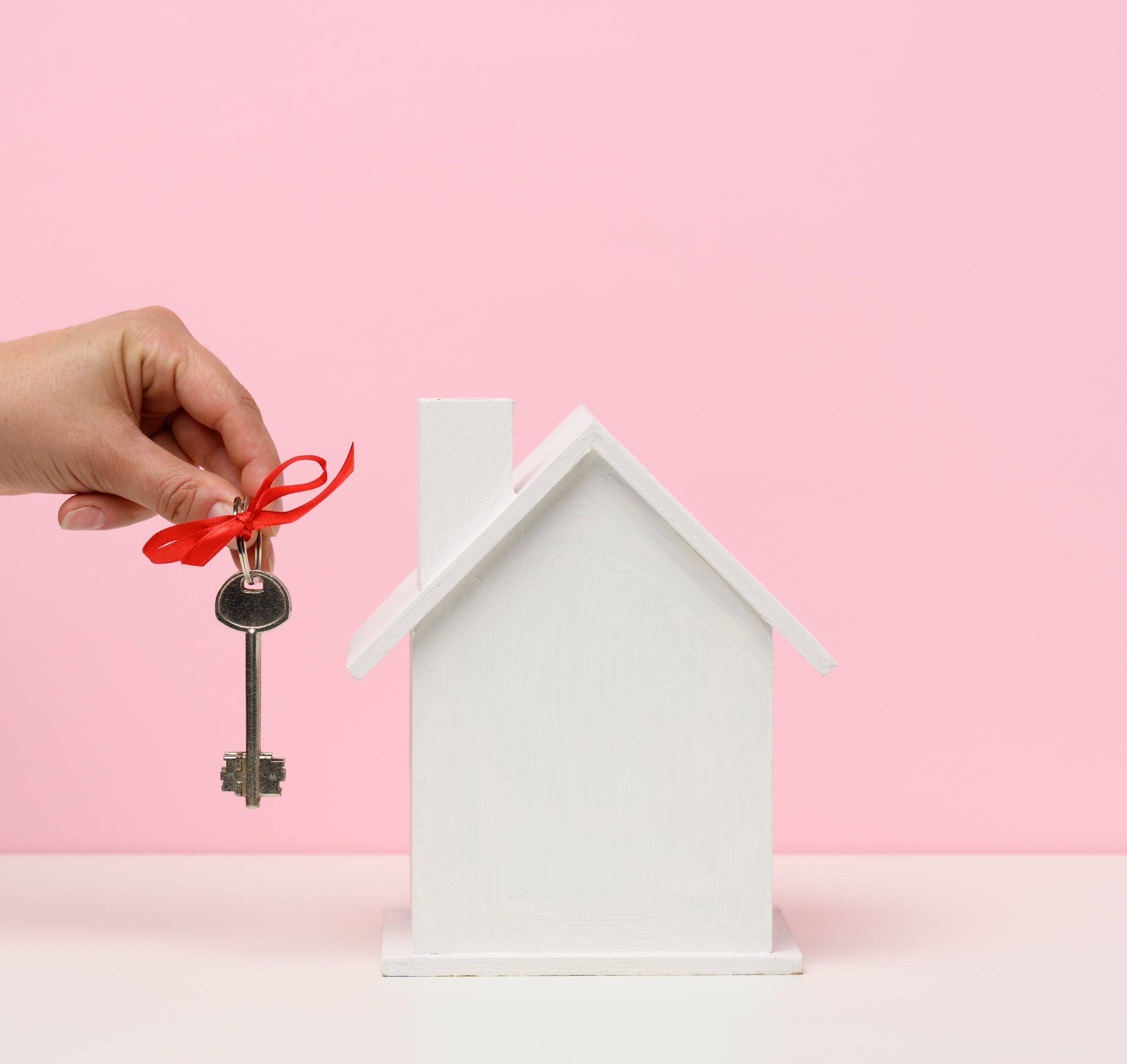 hand holds keys and wooden house on a pink background. Real esta